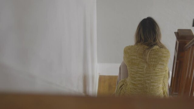 The back of a dejected woman is seen as she sits on the stairs 