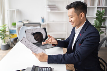 Happy young Asian businessman and woman shaking hands to congratulate successful collaboration on business deal with documents and laptop on table in the office.