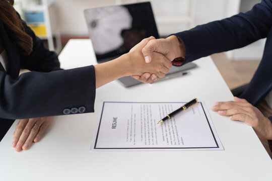 Young happy woman applying for job and giving she's CV to a manager during the interview and shakehand in the office. 