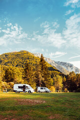 Two camper vans in a camping with amazing landscape views of forest and mountains during sunset. Van road trip holiday and outdoor summer adventure. Nomad lifestyle concept