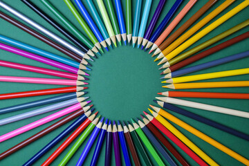Color pencils laid out in circle on green background. Arrangement of multicolored pencils. Top view. Close-up. Selective focus.