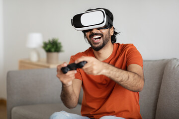 Cheerful young middle eastern guy in vr glasses and casual plays online game on computer with...