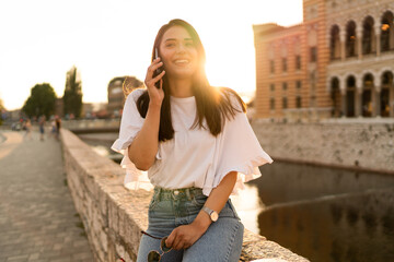 Fototapeta premium The laughing young woman is talking on the phone at night with city lights in the background 