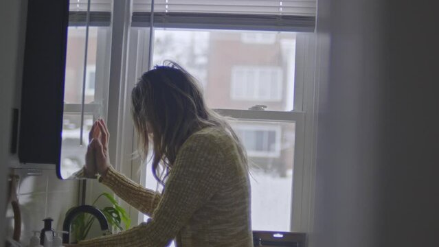 A depressed woman braces herself against the bathroom mirror