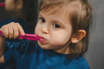 Close-up portrait of a cute little baby girl wearing blue t-shirt holding toothbrush and learn to brushing teeth in the morning at home. Tooth care for children