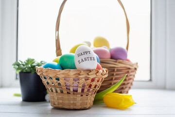 Wicker baskets with bright colorful eggs and with text Happy Easter and flower
