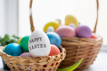 Wicker baskets with bright colorful eggs and with text Happy Easter and flower