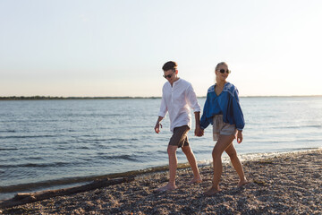 Happy young couple walking on the beach during sunset, prepairing for picnic.