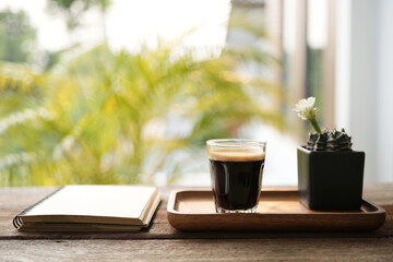 coffee glass cup and white cactus flower in a black pot on wooden table with notebook