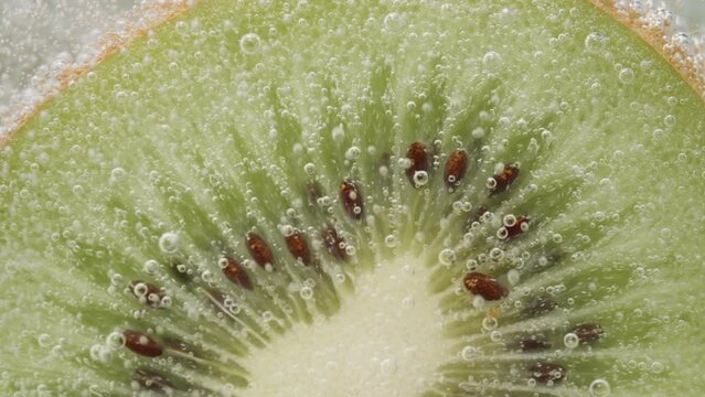 Bubbles slowly rise from the kiwi in the soda. Macro, slow motion. Pano