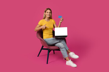 Glad mature european blonde female sit in armchair point finger at laptop, show credit card