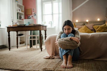 Teenage girl sitting on the floor with head on her knees, koncept of mental health.