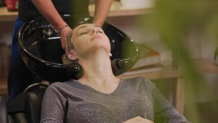 Closeup relaxed female client getting her hair washed in a salon with her eyes closed. Barber gently massaging her head. High quality 4k footage
