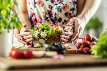 A man and a woman prepared a healthy spring salad. Together they hold a bowl of healthy food with their hands