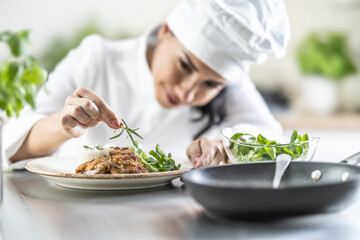 A young female chef finishes a meal with a sprig of rosemary in a restaurant kitchen