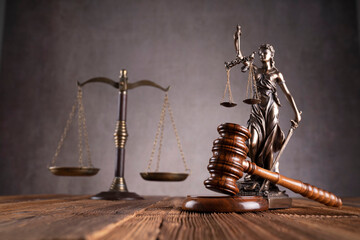 Law symbols composition. Gavel, scale and Themis sculpture on the rustic wooden desk. Gray background.