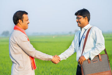 Happy village farmer greeting banker by hand shake by showing paddy field - concept of financial...