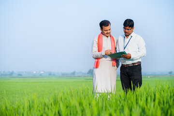 Banker or officer checking loan documents from village farmer at green paddy field - concept of...