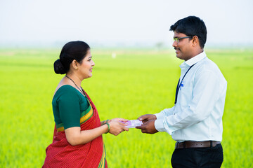 Happy smiling Indian woman receiving money from banker at paddy farmland - concept of financial support, employment and agribusiness