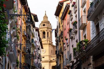 Pamplona, Navarra, SPAIN. The beautiful streets of the city of Pamplona. Beautifully coloured buildings with flowers of different colours, hanging from the balconies. Church tower in background 