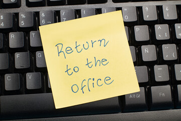 Nota adhesiva post it con un mensaje de regrese a la oficina sobre un teclado de computadora negro....