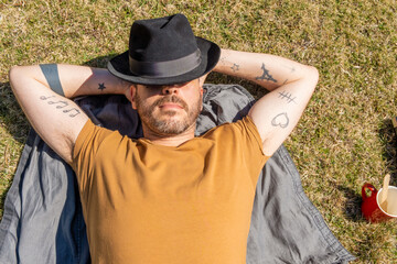 portrait of tattooed man resting taking a nap outdoors while the sun shines on him
