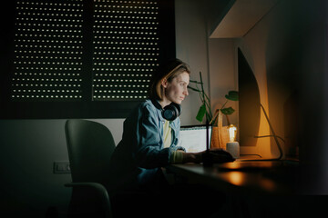 A woman sitting at her desk, either in a cozy office or at home, intently focused on her computer screen while working at night. relaxed and focused