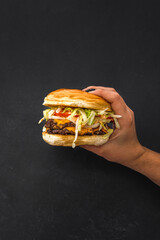 hand grabbing cheeseburger with toppings in an isolated black background. hamburger with cheese,...