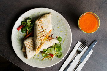 Top Down View of Wrapped Burrito with Beans and Vegetables on a Plate, carrot juice on the table