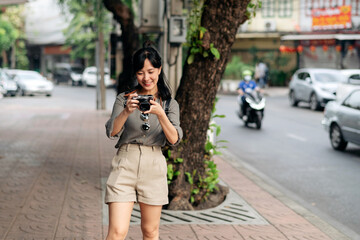 Fototapeta premium Young Asian woman backpack traveler using digital compact camera, enjoying street cultural local place and smile. Traveler checking out side streets.