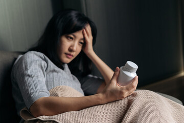 Asian woman with cold and flu reading instructions on medicine bottle