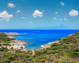 Fototapeta na wymiar Summer stony sea coast landscape with Atthos mount view in far (Halkidiki, Sithonia, Greece).