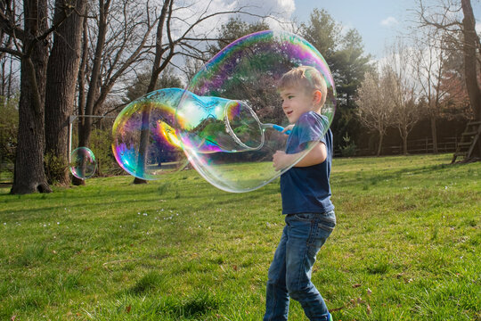 Young boy has fun making giant bubbles outside in a yard