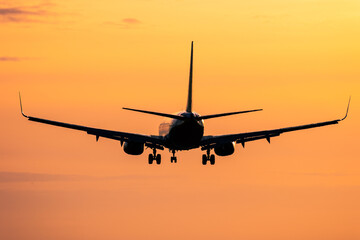 Fototapeta na wymiar Silhouette of airplane in flight against orange sunset sky