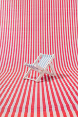 Wooden beach chair on red and white striped background. Minimal summer vacation concept.