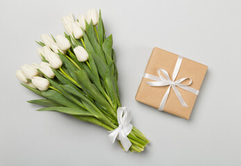 White tulip bouquet and gift box on color background, top view