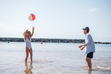 Senior couple playing beach ball on the beach shore and enjoying a fun day at their retirement....