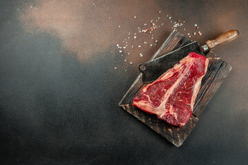 Large raw t-bone steak on a wooden board. Porterhouse steak with a meat cleaver on a dark...