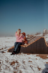 Girl in pink jacket sits with a dog on a bench in winter
