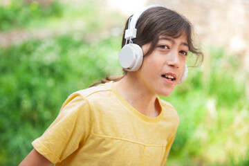 Boy listening to music with white headphones outside next to a green meadow.