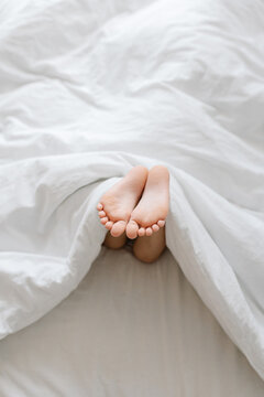 Feet of little girl on bed under white blanket, sleep at morning.