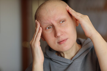 Fototapeta premium Bald woman touching head with fingers, suffering from headache after chemotherapy. Unhappy hairless cancer sick female having migraine at home. Oncology concept. Healthcare,medicine