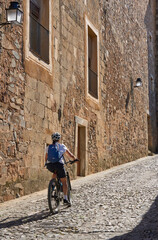 Fototapeta na wymiar cheerful senior woman cycling with her electric mountain bike in the medieaval and moorish downtown of Caceres, Extremadura, Spain