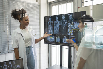 Team of female medical scientists presenting in brain research laboratory by monitor showing MRI,...