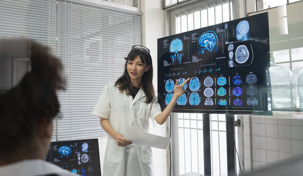 Female medical scientists presenting in brain research laboratory by monitor showing MRI, CT scans brain images. Female doctor wear uniform showing magnetic resonance image (MRI) of brain project
