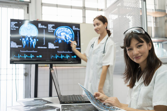 Team of female medical scientists presenting in brain research laboratory by monitor showing MRI, CT scans brain images. Female doctor showing magnetic resonance image (MRI) of brain project