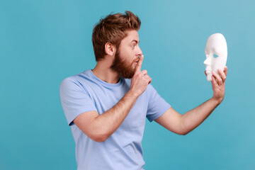 Side view portrait of mysterious handsome man holding white mask in hands and showing shh gesture...