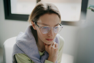 a closeup of a young woman wearing glasses working on a desktop computer in a cozy home office while enjoying the natural light sitting in a bright and airy room 