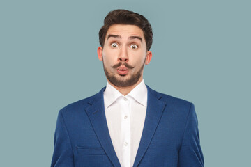 Wow. Portrait of shocked surprised man with mustache standing looking at camera with big eyes, sees something amazed, wearing official style suit. Indoor studio shot isolated on light blue background.