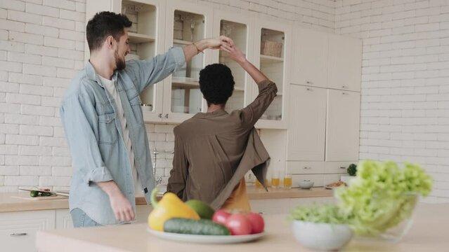 young happy mutinous couple dancing in the kitchen near the table with vegetables and salads
